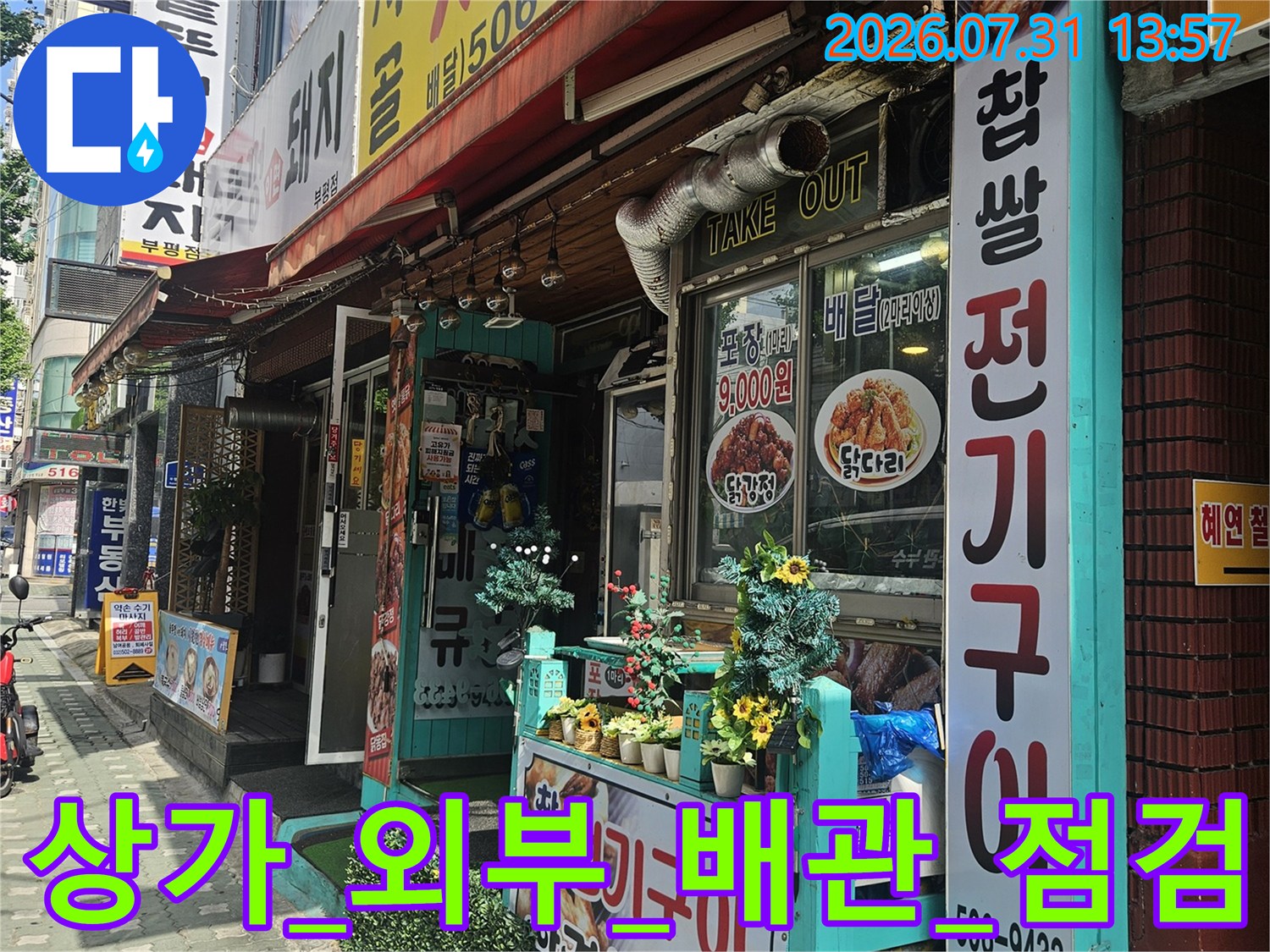 상가 외벽에 노출된 파란색 배관과 안내 표지판이 있는 현장 모습