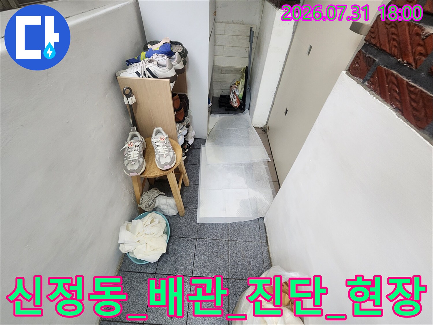 복도형 건물의 입구와 지하 계단으로 이어지는 통로에 놓인 신발과 배관 점검용 도구들
