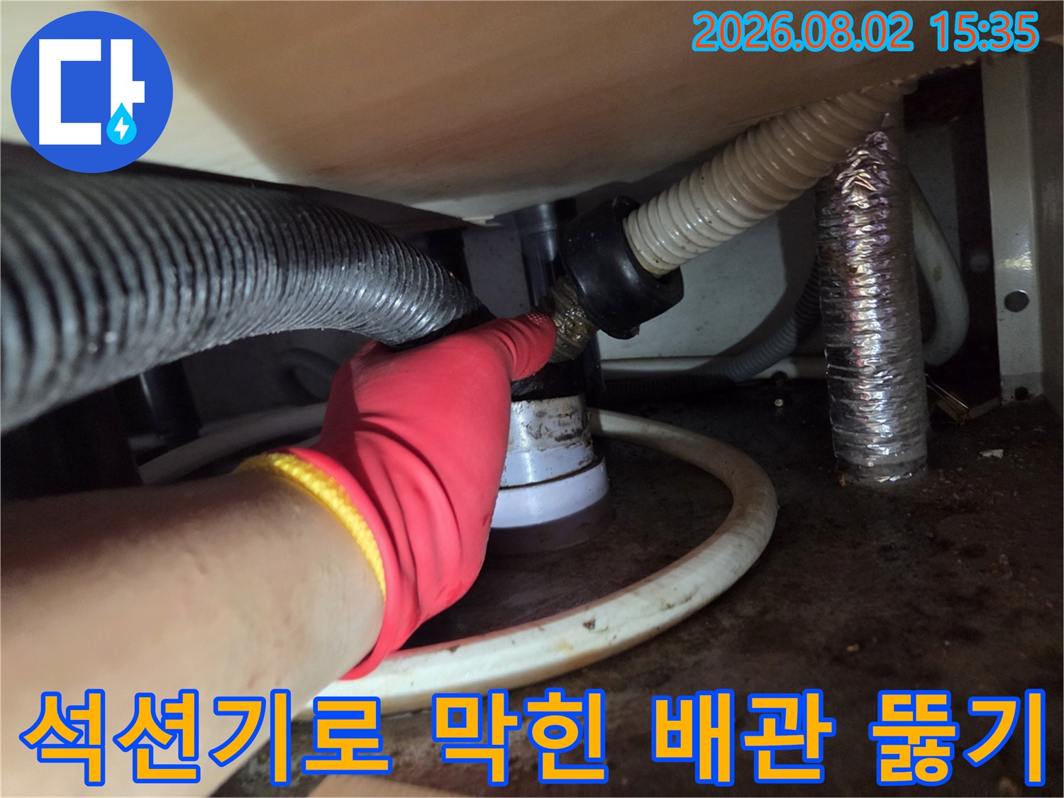 빨간 장갑을 끼고 싱크대 하단 배수 호스를 석션 장비로 청소하는 기술자의 모습