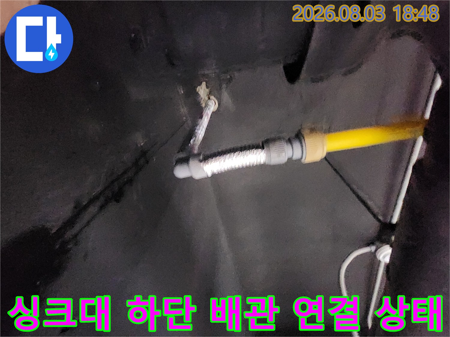 노란색 파이프와 금속 호스가 겹쳐진 싱크대 밑 공간의 모습