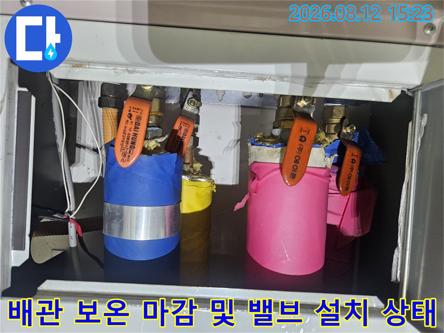 금속 케이스 안에 파란색과 분홍색 보온재로 감싸진 배관과 주황색 밸브들이 있는 모습