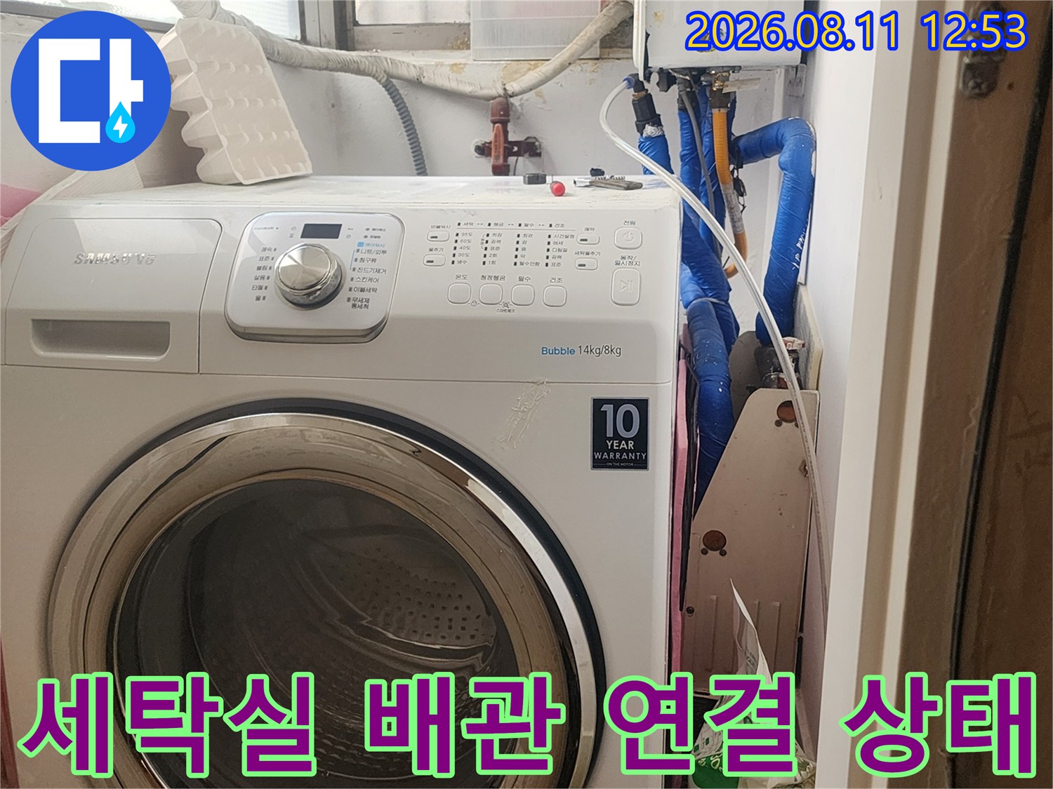 세탁기 뒤편 파란색 수도 배관과 보일러 장치가 노출된 현장 사진입니다.
