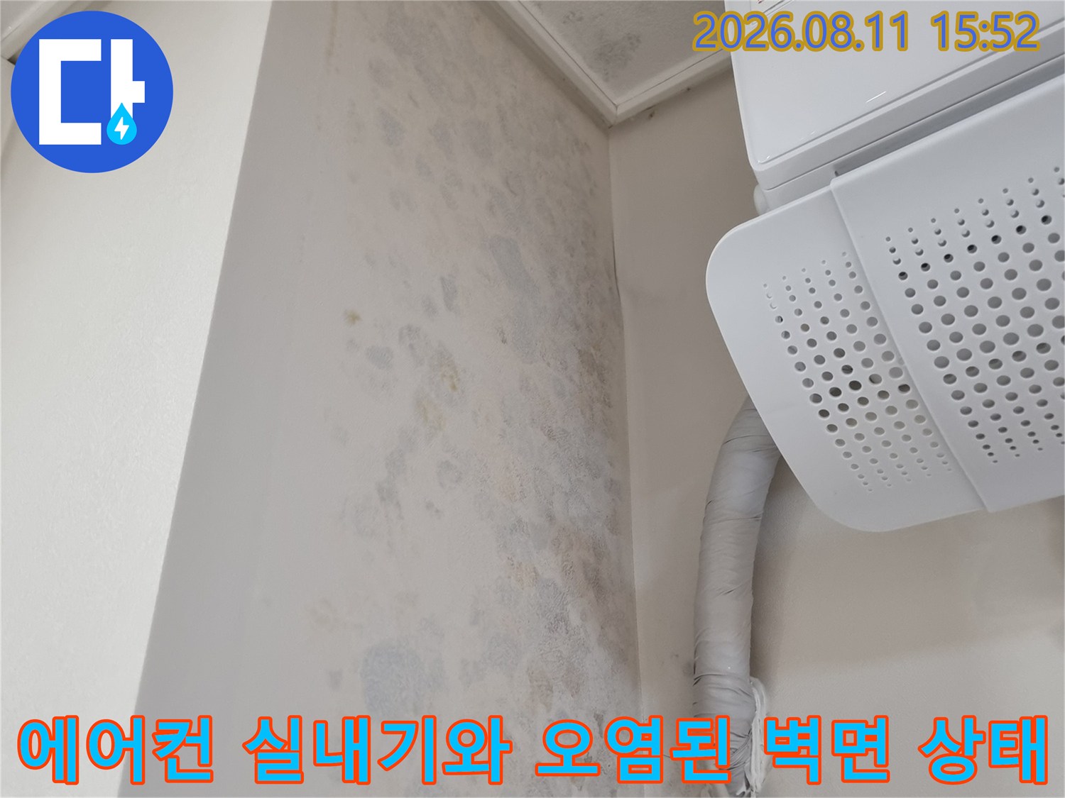 천장 구석에 설치된 에어컨과 그 옆으로 지나가는 흰색 배관 그리고 벽지에 핀 곰팡이 얼룩