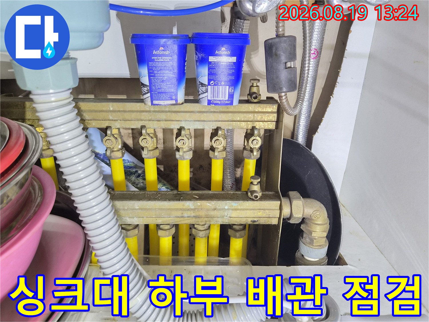 싱크대 아래쪽의 복잡한 배관 구조와 분배기를 촬영한 이미지입니다.