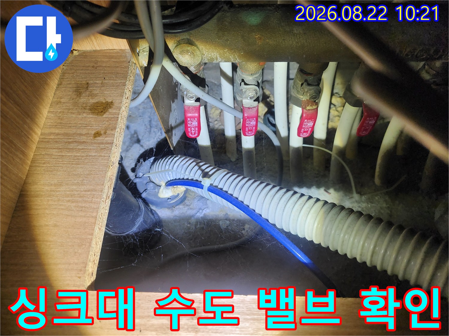 붉은색 손잡이가 달린 수도 밸브와 흰색 배수 호스가 복잡하게 연결된 배관 구조입니다.