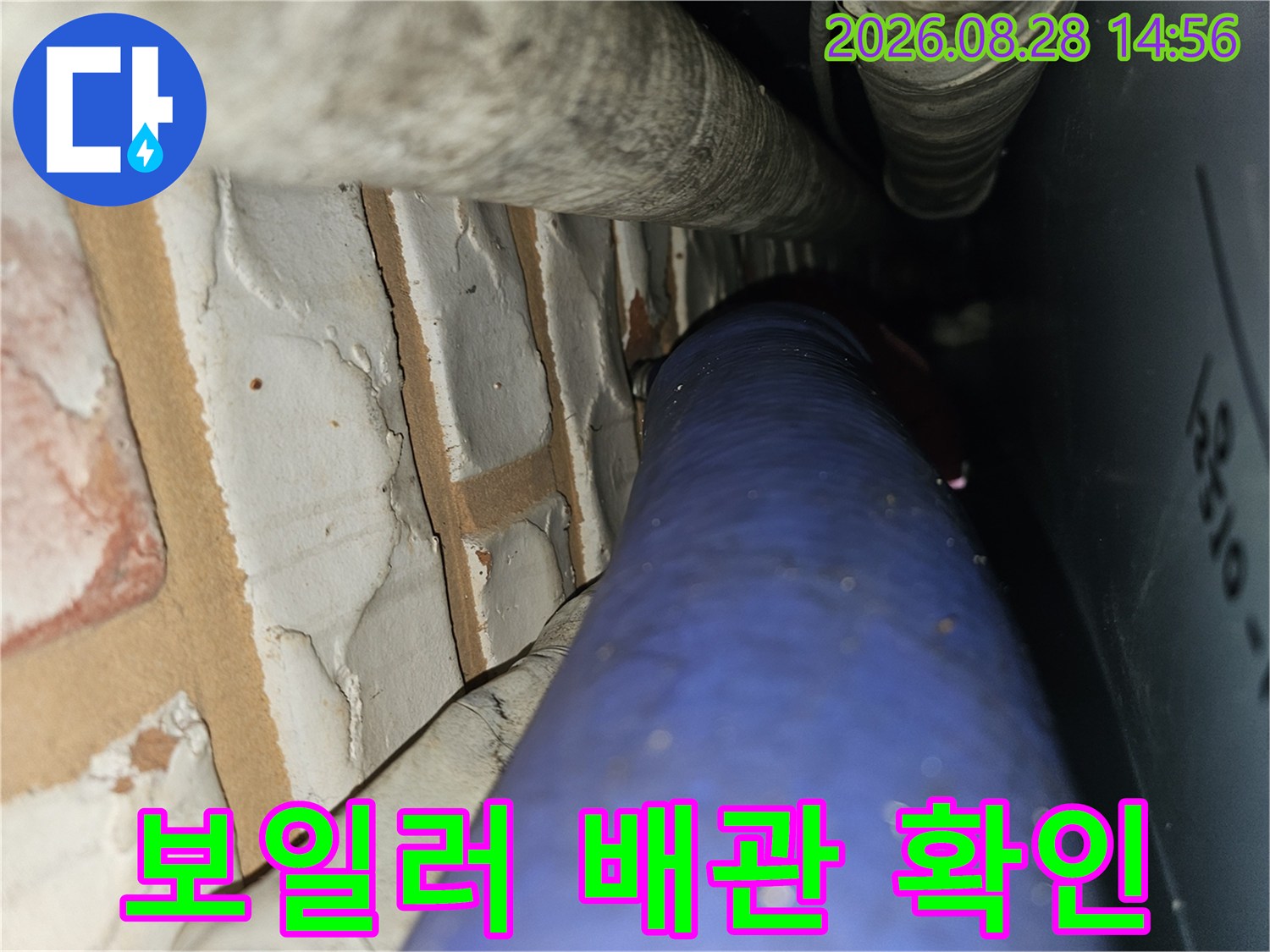 벽돌 벽면의 굴곡진 부분에 위치한 파란색 배관과 상단 보온 배관 사진입니다.