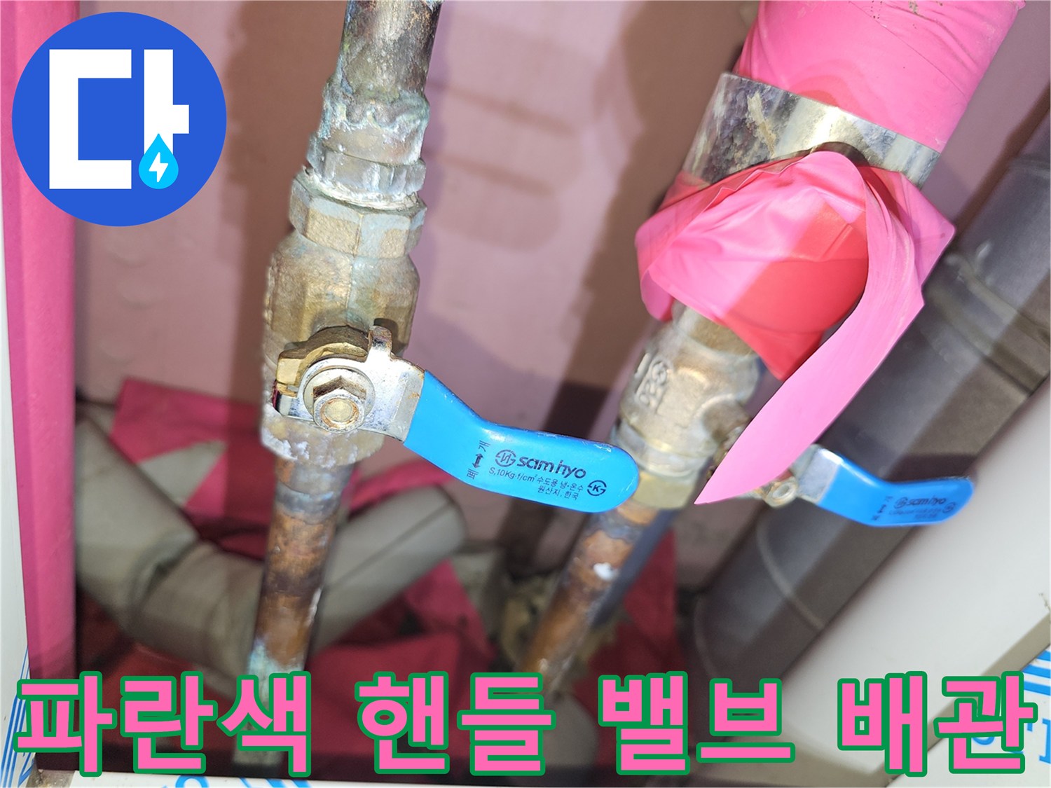 노후된 금속 배관에 설치된 파란색 조절 밸브의 모습입니다.