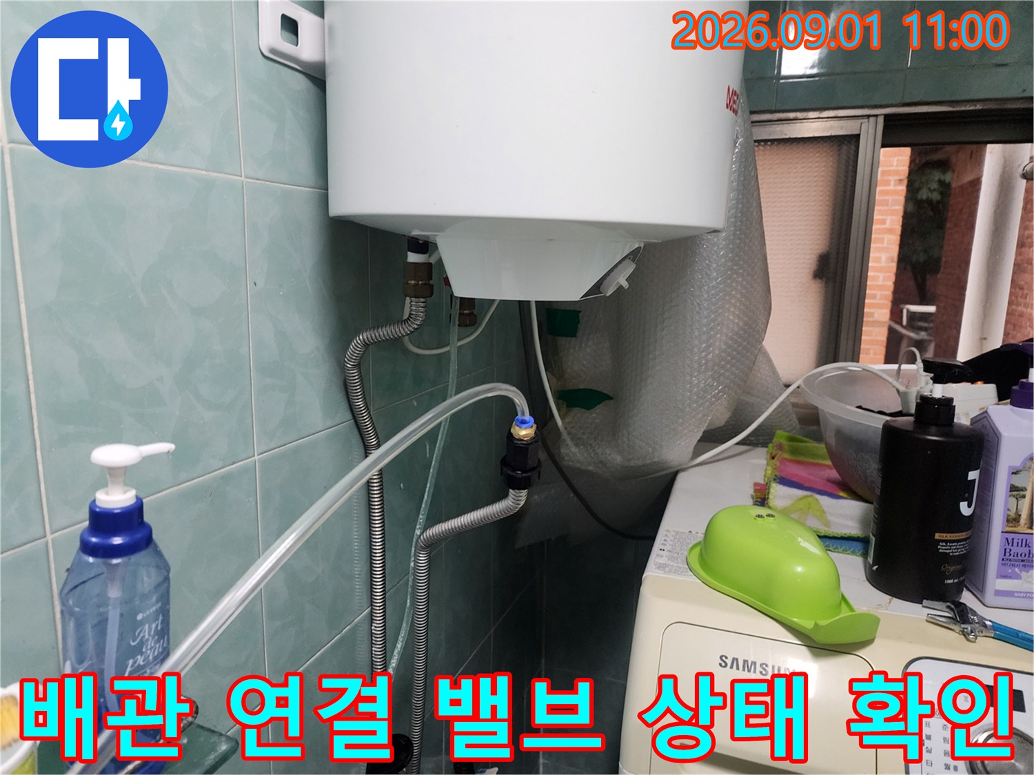 온수기 아래쪽 금속 배관과 밸브의 연결 상태를 촬영한 사진입니다