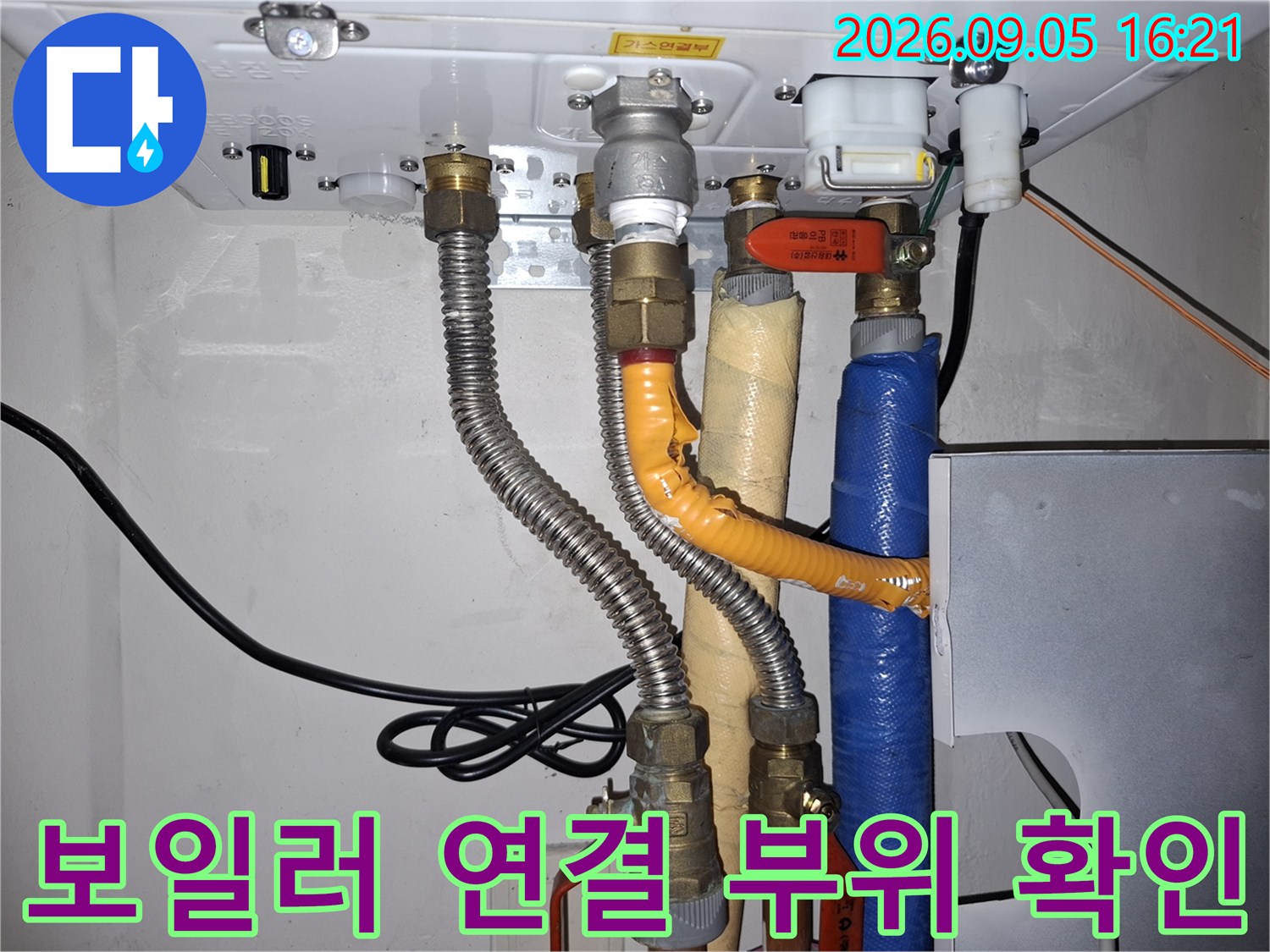 보일러 하단에 연결된 주름관과 밸브류의 상태를 면밀히 관찰하고 있습니다.