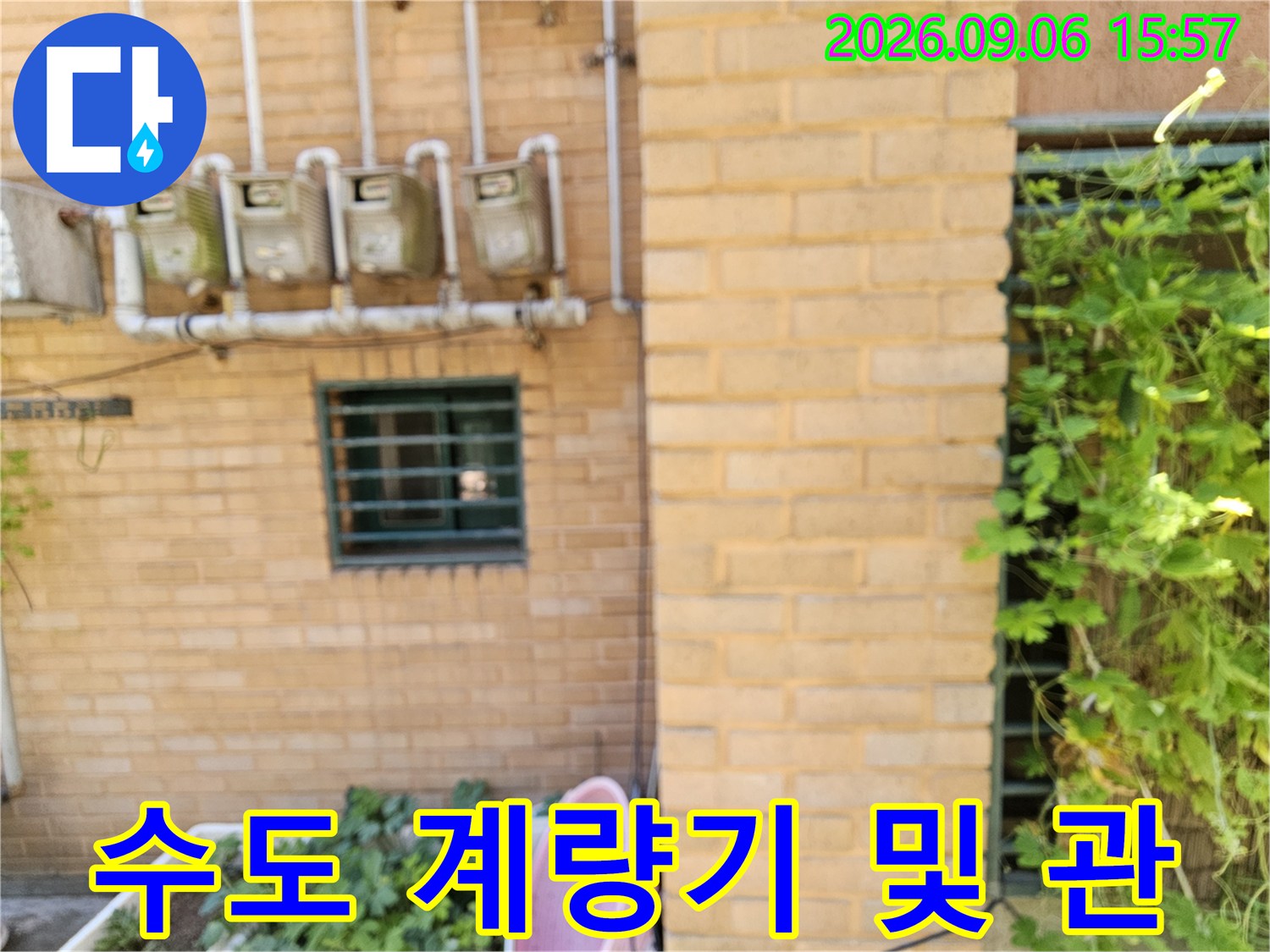 건물 외벽 벽돌 구조물에 설치된 수도 계량기와 상단 배관 라인