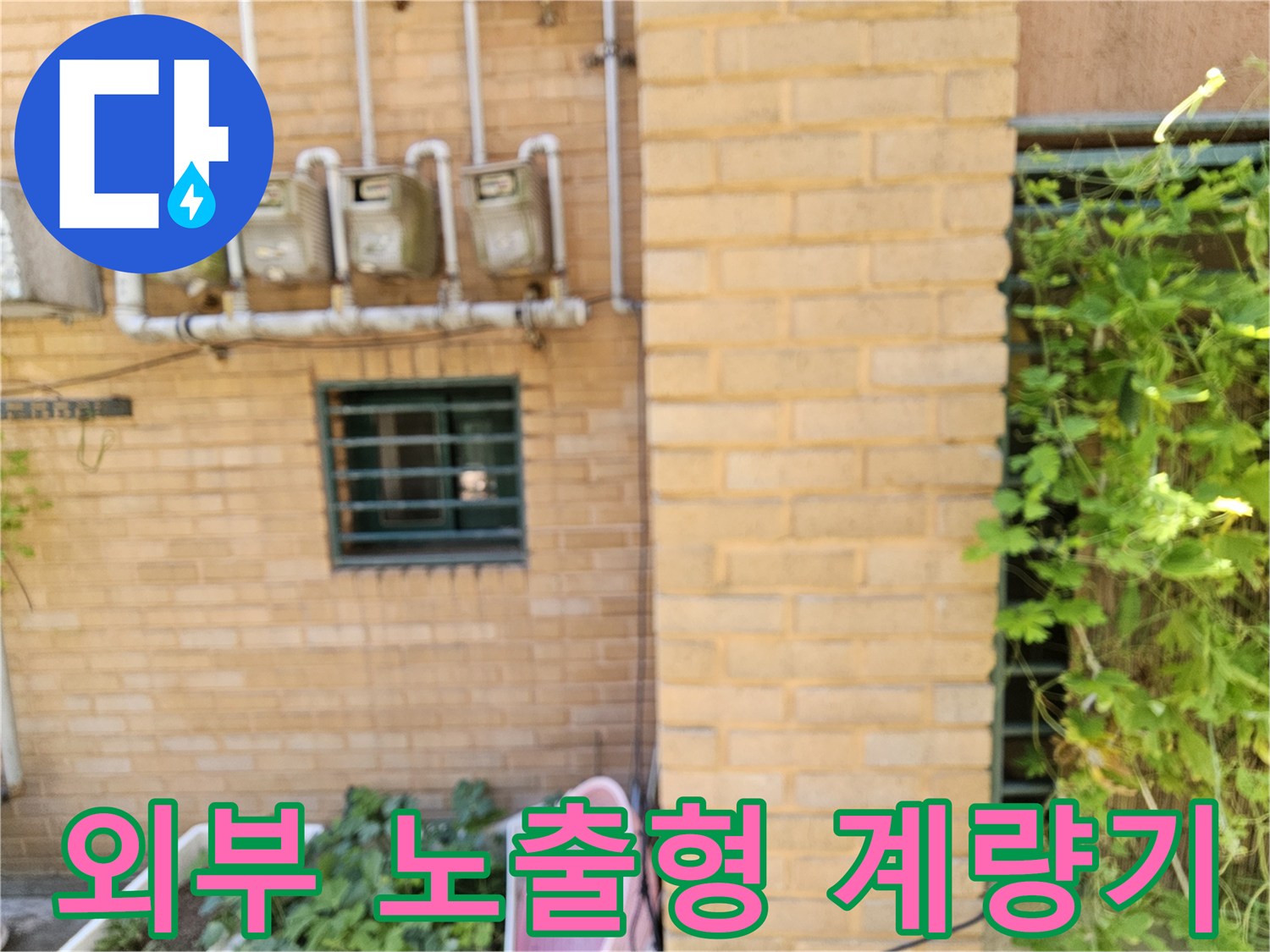 노란 벽돌 외벽에 설치된 수도 계량기와 연결 배관 모습입니다.