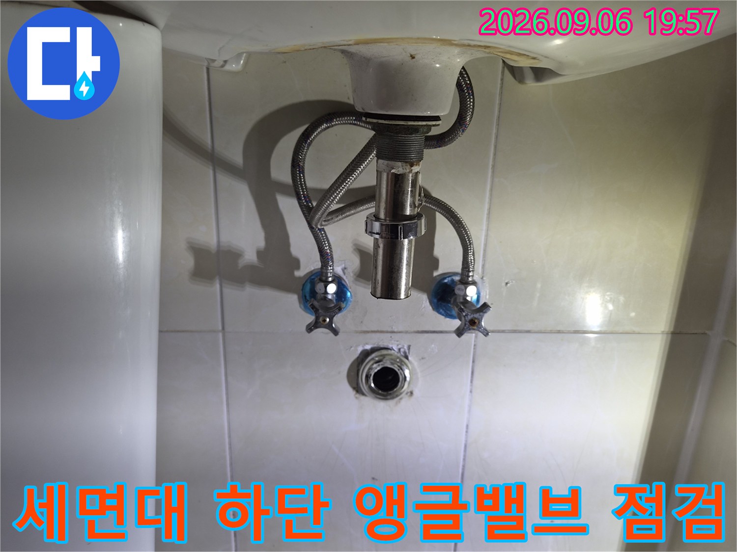 세면대 아래쪽의 은색 배관 호스와 밸브 연결 부위 모습입니다.