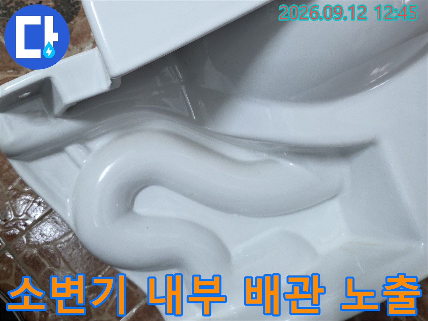 탈거된 소변기 안쪽의 노출된 배관과 바닥 타일 경계 부위
