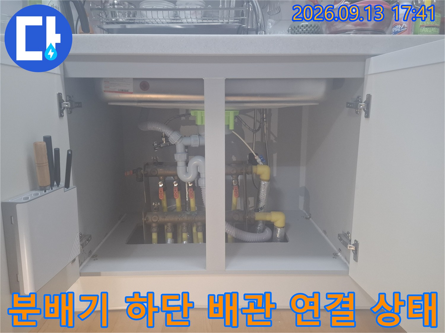 싱크대 아래 보일러 분배기와 노란색 배관이 얽혀 있는 모습입니다.