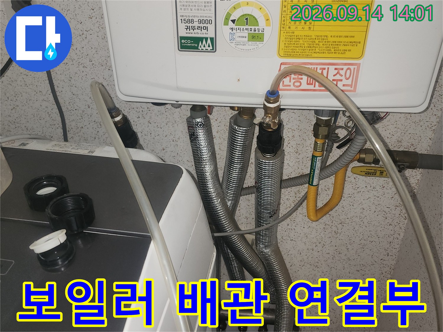 보일러 하단에 연결된 금속 재질의 급수 및 온수 배관 상태를 점검하고 있습니다.