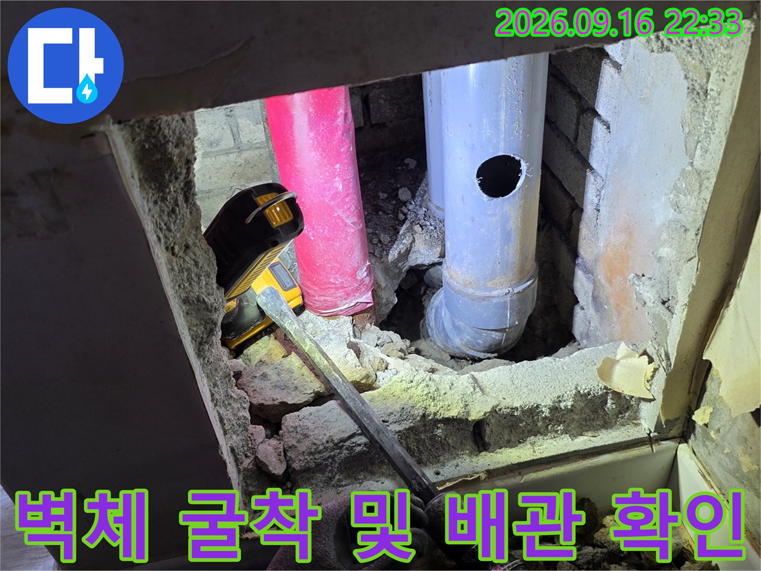 벽 내부의 분홍색과 회색 배관이 드러난 굴착 현장 이미지입니다.